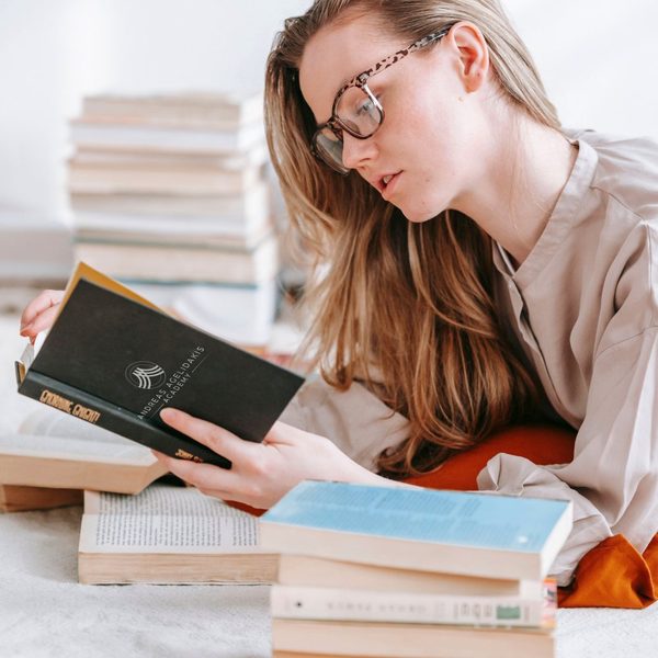 Eine Frau liest ein Buch, um sie herum Stapel weiterer Bücher